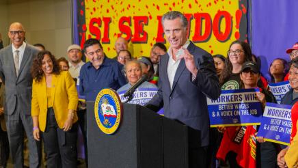Gov. Newsom at podium, speaking, with bill supporters standing behind