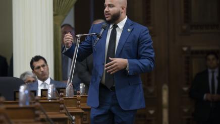 Asm. Bryan standing and speaking into microphone on the Assembly Floor