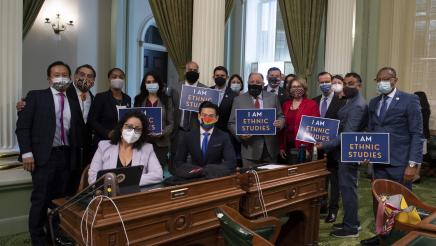 Group photo of assemblymembers holding "I AM ETHNIC STUDIES" signs
