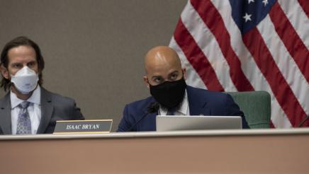 Asm. Bryan, seated, speaking into microphone as committee member listens on