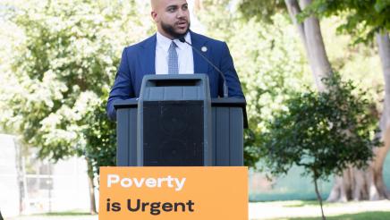 Asm. Bryan at podium, speaking with informational sign at front