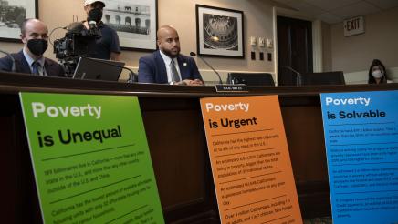 Asm. Bryan seated with factual signs about poverty at front