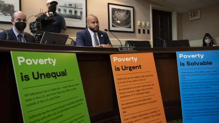 Asm. Bryan seated with factual signs about poverty at front