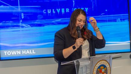 Guest speaker at podium, speaking to audience, with screen in background