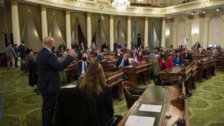 Asm. Bryan at microphone, speaking, as fellow assemblymembers listen on