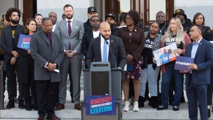 Asm. Bryan at podium, speaking, with supporters in background