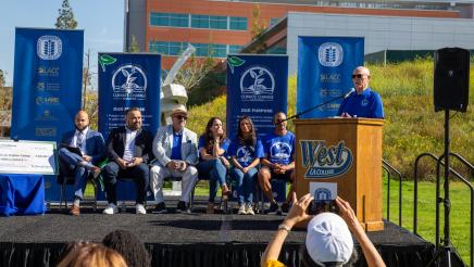 Guest speaker at podium, speaking, while fellow speakers listen on