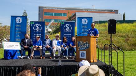 Guest speaker at podium, speaking, while fellow speakers listen on