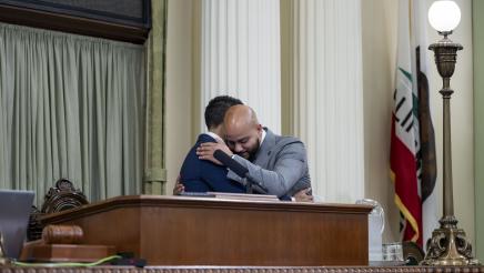 Asm. Bryan and Speaker Rivas hugging behind the podium on the Assembly Floor