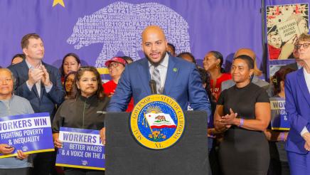 Asm. Bryan at podium, speaking, with bill supporters standing behind