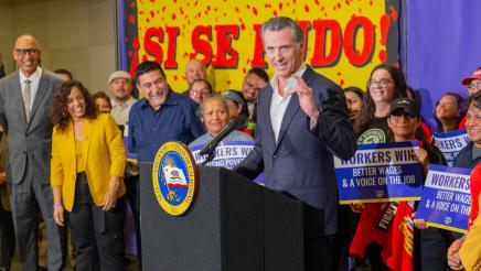 Gov. Newsom at podium, speaking, with bill supporters standing behind