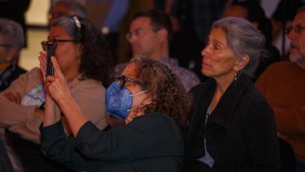 Audience members listening attentively, one taking a photo