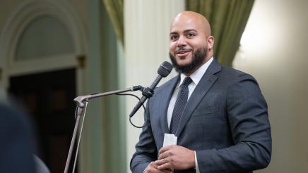 Asm. Bryan standing and speaking into microphone on the Assembly Floor