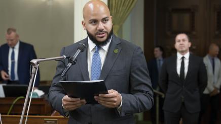 Asm. Bryan standing on Assembly Floor, speaking into microphone