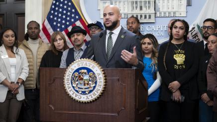 Asm. Bryan at podium, speaking, with supporters at either side