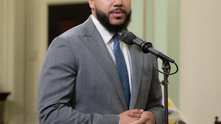 Asm. Bryan standing and speaking into microphone on the Assembly Floor