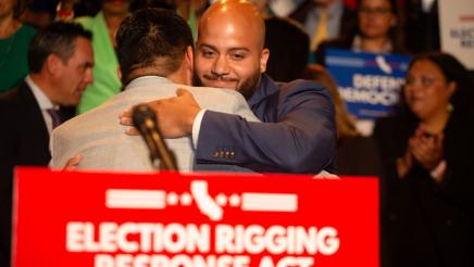 Asm. Bryan at podium, hugging fellow legislator