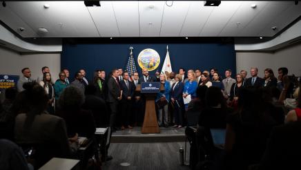 Wide view of Asm. Bryan at podium, speaking, while fellow legislators listen on