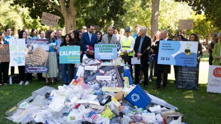 Asm. Bryan at podium, speaking, with recyclables piled in foreground