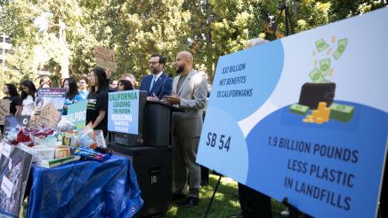 Asm. Bryan at podium, speaking, with informational poster board at right