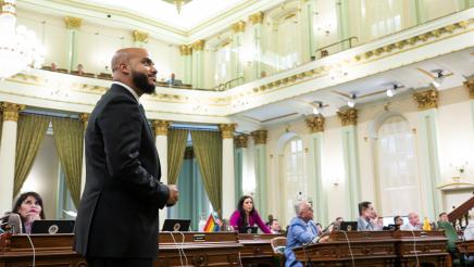Asm. Bryan standing on the Assembly Floor, looking toward the front of the chamber